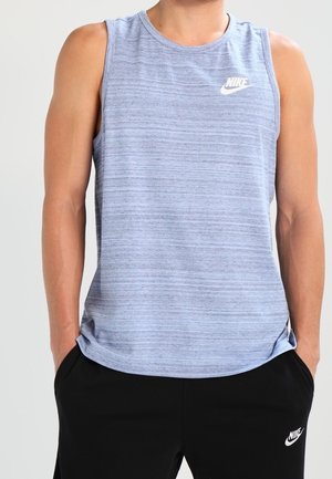 Ärmelloses hellblaues Nike-Shirt mit dezenten Streifen, getragen mit schwarzen Nike-Hosen, Hände in den Taschen, Oberkörper und obere Beine sichtbar.