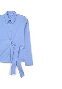 Camicia a maniche lunghe azzurro chiaro realizzata in tessuto morbido, con colletto a punta, chiusura con bottoni sul davanti e un dettaglio annodato sul lato sinistro.