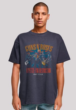 Black graphic t-shirt featuring a vintage design of band members, text "GUNS N' ROSES" and "APPETITE FOR DESTRUCTION," 1987 Tour.