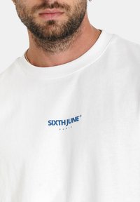 Witte katoenen sweatshirt met een ronde hals en een blauw bedrukte logo "SIXTH JUNE" op de linkerkant van de borst. Zachte textuur.