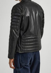 Svart skinnjacka med vadderade axel- och sidpaneler, en slät yta, en åtsittande design och dragkedjor vid ärmsluten.