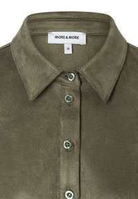 Olivgrünes, strukturiertes Stoffhemd mit spitzem Kragen. Verfügt über entsprechende grüne Knöpfe und ein Etikett mit "MORE & MORE" und Größe 36.