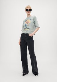 Lysegrønn kortermet grafisk t-skjorte med blomstertrykk, parret med høy midje sorte vide jeans og spisse sorte sko.