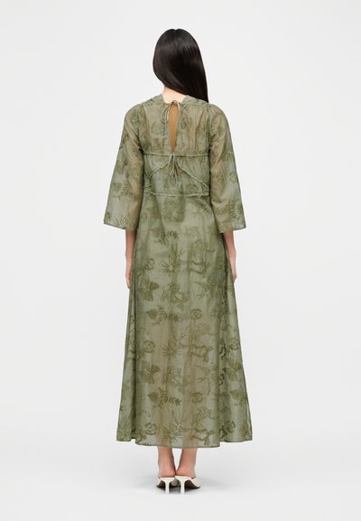 Μακρύ, ελιάς πράσινο φόρεμα με κεντητά σχέδια με λουλούδια και πουλιά. Διαθέτει στρογγυλή λαιμόκοψη, μακριά μανίκια και δέσιμο στο πίσω μέρος.