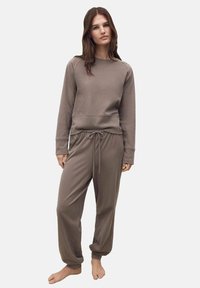 Completo loungewear marrone composto da una felpa con collo rotondo e maniche raglan e pantaloni della tuta con coulisse e vestibilità rilassata. Tessuto morbido.