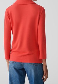 Haut rouge à manches longues avec un large col, texture douce et coupe décontractée, associé à un jean en denim bleu. Vue arrière montrant la forme de la chemise.