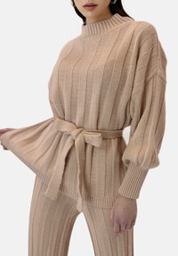 Beżowy sweter dzianinowy i pasujące spodnie w pionowe paski, z wysokim dekoltem i paskiem w talii, wykonane z teksturowanej, miękkiej tkaniny.