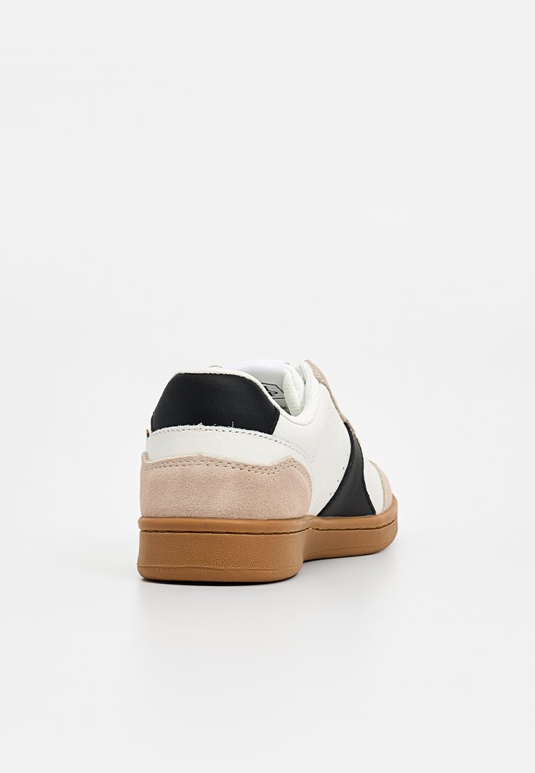 Weiße Sneaker mit schwarzen und beigen Wildlederpaneelen, braune Gummisohle, von hinten auf einem weißen Hintergrund betrachtet.