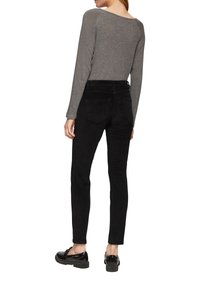 Pantalons en velours côtelé noirs, coupe slim, avec une taille mi-haute et deux poches arrière. Associés à un haut ajusté gris à manches longues et des chaussures noires.
