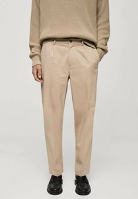 Beige broeken met een rechte snit en twee voorknofpen, gecombineerd met een gestructureerde gebreide trui en zwarte schoenen.