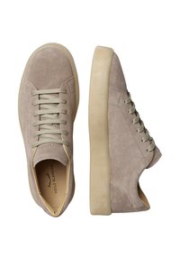 Sneaker in suede beige con punta rotonda, lacci verde chiaro e suola in gomma crema con texture. Presentano cuciture minime e branding discreto.