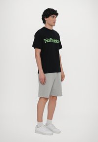 Tricou negru cu text verde "No Problem", asociat cu pantaloni scurți gri și adidași albi. Design simplu, croi lejer, mâneci scurte.