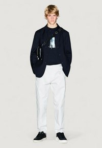 Blazer blu navy su una t-shirt grafica nera, pantaloni bianchi e sneakers nere. Include una borsa a tracolla nera, con texture lisce e colori a contrasto.