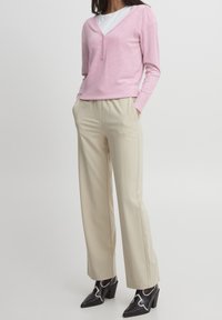 Top de punto de manga larga en rosa claro con escote en V y detalle de botones, combinado con pantalones de pierna ancha en beige y zapatos de tacón negros con acentos blancos.