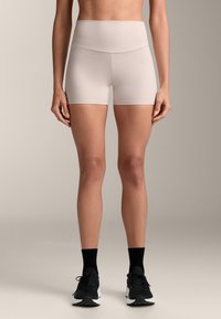 Svetlo béžové šortky s vysokým pásom, hladkou textúrou, priliehajúcim strihom a dĺžkou do polovice stehien. Nosené s čiernymi teniskami a ponožkami.