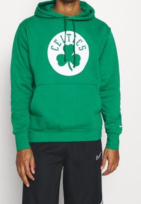 Hoodie vert avec un motif rond blanc représentant un trèfle et le texte "CELTICS" au-dessus. Fabriqué en matériau doux, il possède une poche avant et des cordons de serrage.