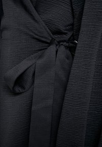 Gros plan sur une robe en tissu texturé foncé avec une ceinture nouée à la taille et des manches longues.