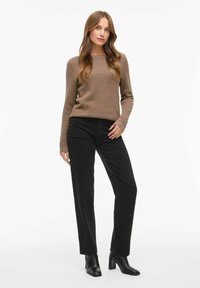 Maglione marrone a trama con maniche lunghe abbinato a pantaloni neri a gamba dritta e stivaletti neri con tacco, su uno sfondo bianco.