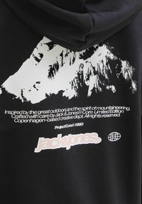 Čierna mikina s kapucňou a bielym grafickým motívom hory spolu s textom odkazujúcim na horolezectvo, branding Jack & Jones Core Limited Edition a ikonu globusu.
