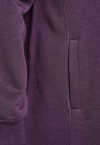 Lila sweatshirt med ett mjukt, texturerat tyg, sidoficka och sömnadsdetaljer längs sömmarna.