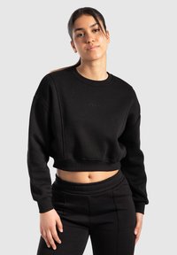 Sweatshirt noir court avec un col rond et des manches longues, présentant une finition texturée et un discret logo sur le devant.