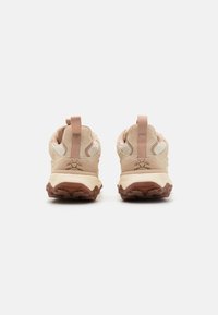 Baskets de sport beige clair avec une tige texturée, un design de soutien à la cheville et une semelle en caoutchouc marron avec un motif de semelle prononcé.