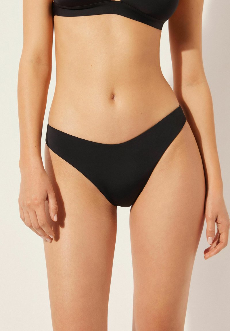 Bas de bikini noir fabriqué en tissu lisse et extensible. Présente un design taille basse avec une couverture minimale et des bords nets.