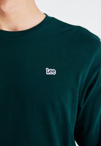 Groene katoenen longsleeve t-shirt met een klein wit geborduurd "Lee" logo op de linkerborst. Ronde hals ontwerp, zachte textuur.