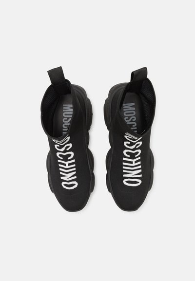 Black slip-on shoes with a snug sock-like fit. Features white "MOSCHINO" text, textile upper, and a chunky rubber sole for durability.