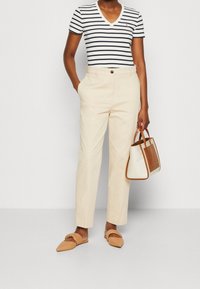 Bílo-námořnické proužkované tričko s V výstřihem, béžové kalhoty na míru, kabelka s hnědými akcenty a světle hnědé slip-on boty.