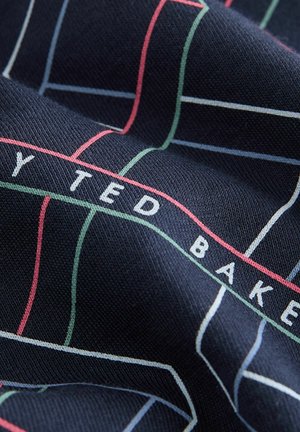 Mornarsko blago z mrežastim vzorcem v beli, rdeči in zeleni barvi ter napisom "TED BAKER" vtkanim v belem, ki prikazuje teksturirano površino.