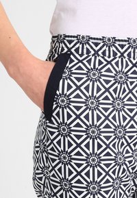 Marinblå och vita mönstrade byxor med geometrisk design, med en enfärgad marinblå fickdetalj och ett elastiskt midjeband för komfort.