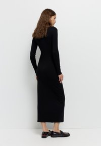 Crna dugosleeve haljina s uskim krojem i dugom dužinom. Glatka tkanina s minimalističkim stilom. U kombinaciji s crnim cipelama.