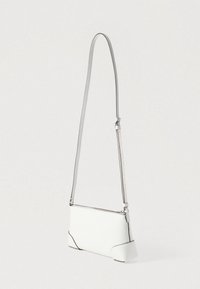 Hvid skuldertaske i læder med tekstureret overflade, sølvfarvet hardware og smalt justerbart rem. Har kontrasterende sort syning og lynlås.