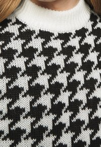 Suéter de punto con un patrón de espiga en blanco y negro, con un acabado texturizado y un cuello acanalado blanco.