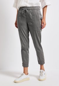 Grå dragsnörpantaloner i mjukt tyg, med sidofickor, avsmalnande mudd och en avslappnad passform. Kompletterat med vita sneakers.