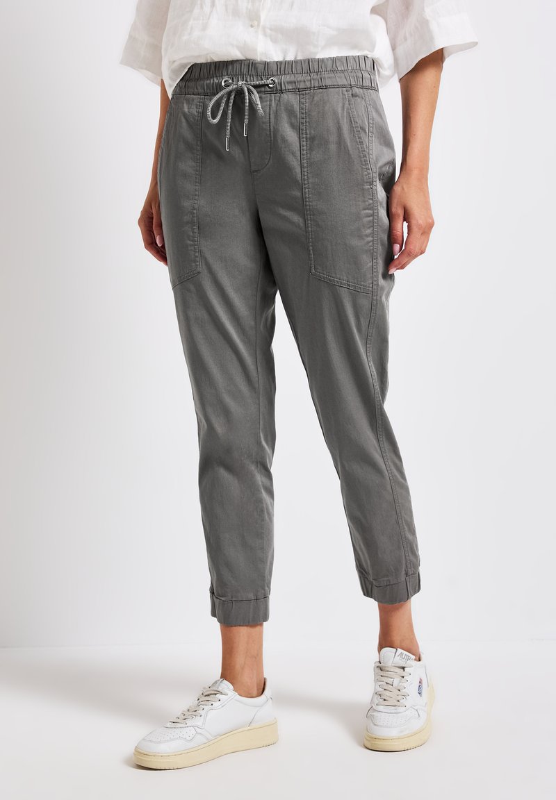 Grå dragsnörpantaloner i mjukt tyg, med sidofickor, avsmalnande mudd och en avslappnad passform. Kompletterat med vita sneakers.