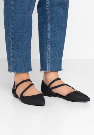 Ballerines noires à bout pointu en matière lisse avec des sangles croisées et un petit talon, associées à un denim à ourlet effiloché.