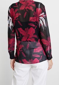 Durchsichtige schwarze Bluse mit auffälligem pinkfarbenem Blumenmuster, langen Ärmeln und geknöpften Manschetten. Leichtes Material mit glatter Textur.