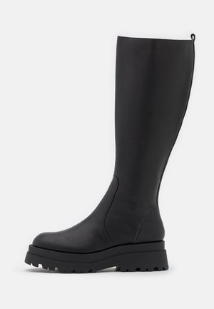 Bottes hautes en cuir noir avec semelle épaisse à crampons et bout arrondi, vue de profil sur un fond clair uni.