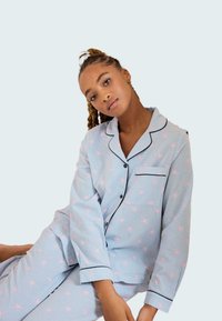 Ensemble de pyjama bleu clair avec un motif d'étoiles roses, design rayé, accents noirs sur le col et la poche, fabriqué en tissu doux.