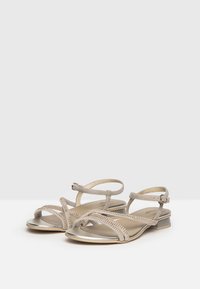 Beige strappy sandals with a metallic silver heel, featuring rhinestone accents across the straps and a soft textured finish.