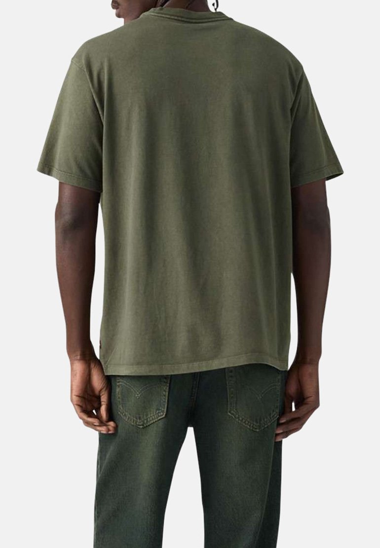 Hombre vistiendo una camiseta de manga corta lisa verde oliva y jeans verdes oscuros a juego, visto desde atrás contra un fondo neutro.