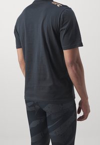 Czarna koszulka z krótkim rękawem o gładkiej fakturze. Na ramieniu znajduje się pomarańczowe logo "UFC". Zestawiona z wzorzystymi ciemnymi legginsami.