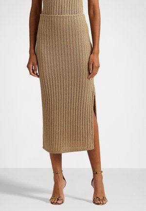 Beige ribbed knit midi skirt with side slit worn with tan snake print ankle-strap sandals on model against white background.