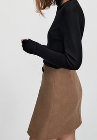 Zwarte coltrui met lange mouwen en duimgaten, gecombineerd met een tan A-lijn rok met een gedefinieerde taille en een gladde textuur.