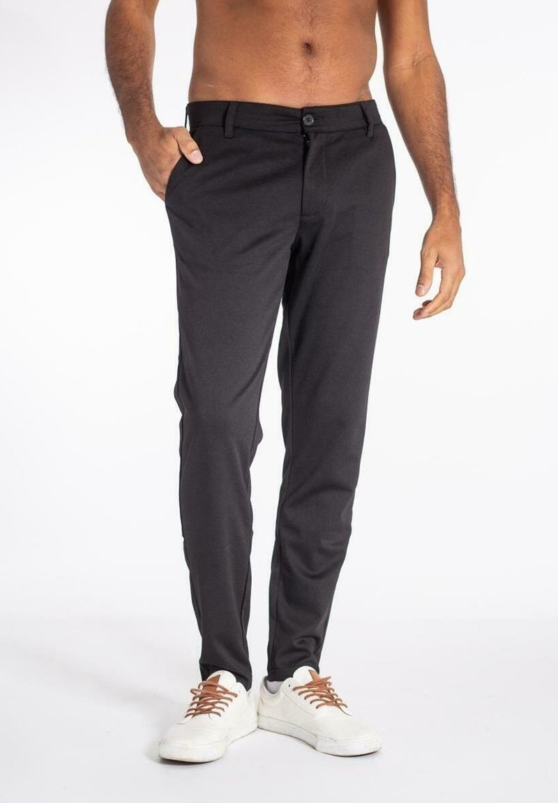 Pantalones negros a medida hechos de tela ligera, con diseño de pierna recta, bolsillos delanteros y cierre de botón. Combinados con zapatos blancos.