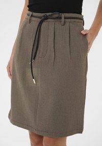 Jupe à carreaux marron en tissu texturé, dotée d'une ceinture noire à cordon de serrage et de poches latérales, coupée au genou avec un design plissé à l'avant.