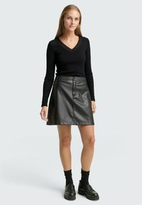 Schwarzes Langarmshirt mit Spitzen-V-Ausschnitt, kombiniert mit einem schwarzen A-Linie-Rock aus Kunstleder, der über einen frontalen Knopfverschluss und Taschen verfügt.