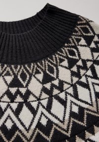Svart och krämfärgad mönstrad jumper med ribbad krage, geometriska mönster och en mjuk textur. Mellantjock stickad konstruktion.